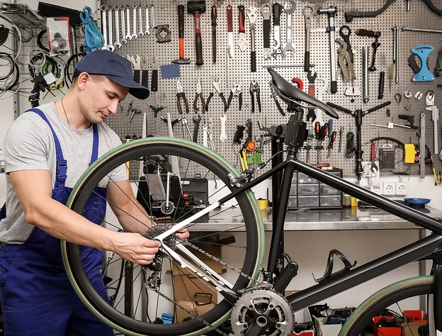 Mécanicien de vélo en combinaison bleue ajustant une roue arrière dans un atelier à Montluçon dans l'Allier 03