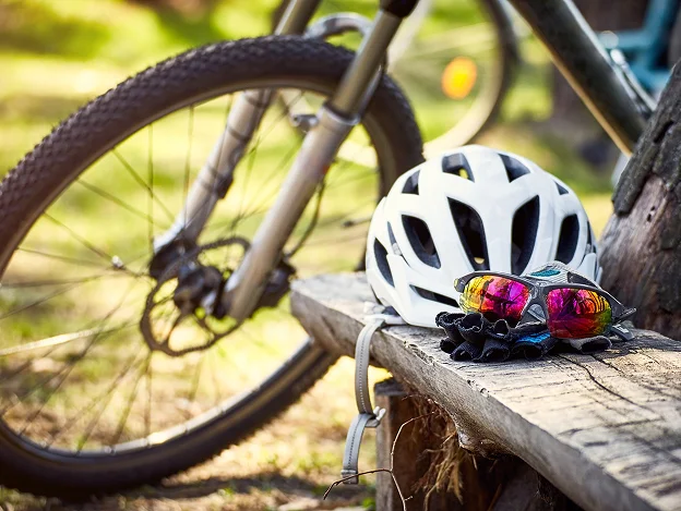 Casque de vélo blanc, lunettes de soleil colorées et gants posés sur un banc en bois à Montluçon dans l'Allier 03