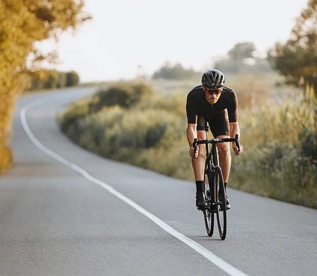 Cycliste en tenue noire sur une route sinueuse bordée d'herbe et d'arbres à Montluçon dans l'Allier 03
